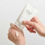 Hand applying a white cream from a container labeled 'Skin&Co' on a light background