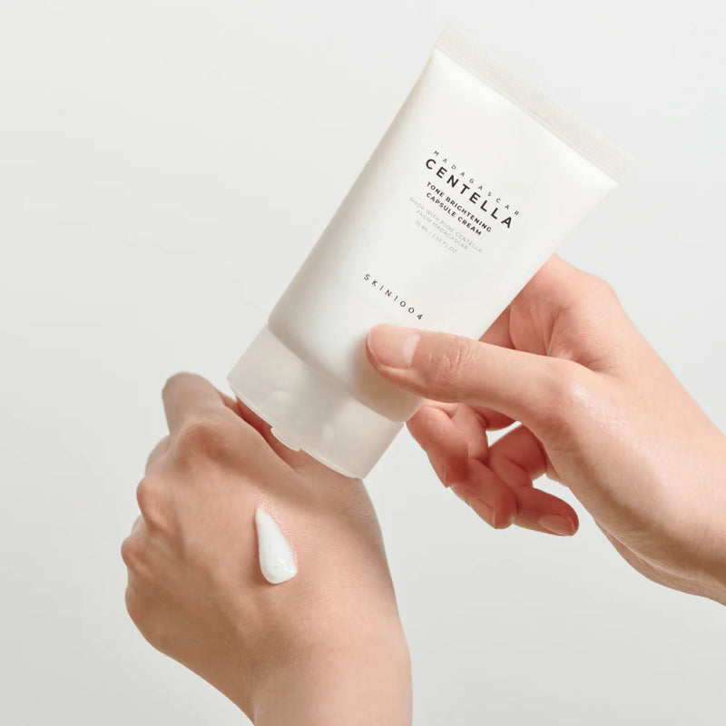 Hand applying a white cream from a container labeled 'Skin&Co' on a light background